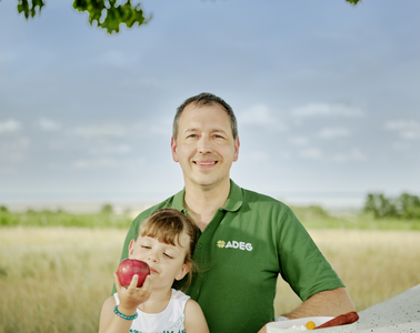 adeg Kaufmann Wolfgang Stadlmann mit seiner Tochter die gerade einen Apfel isst