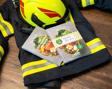 Adeg Kochbuch auf Feuerwehrjacke und Helm